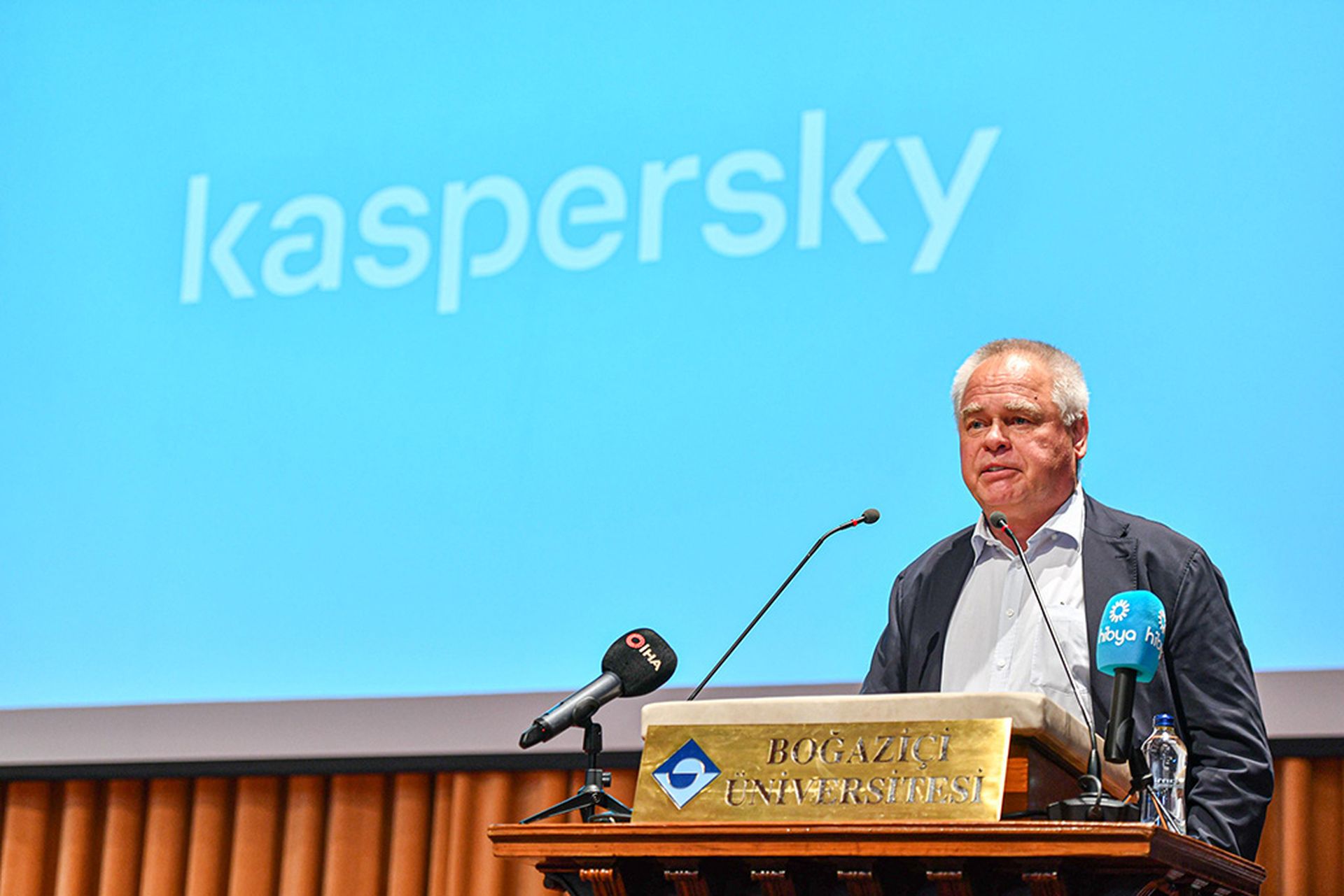 Eugene Kaspersky speaks at a podium in front of a blue screen displaying his company's logo