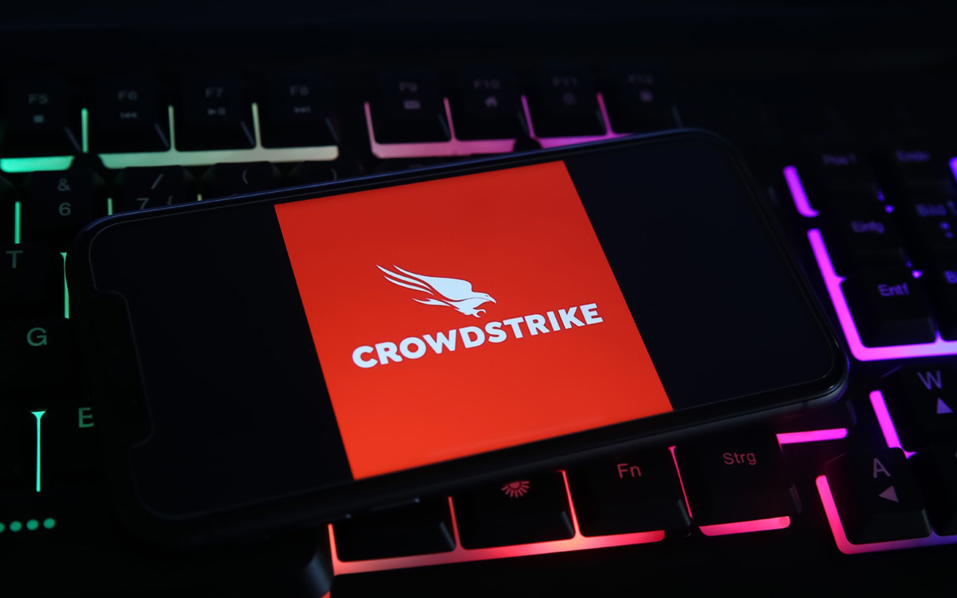Closeup of mobile phone screen with logo lettering of crowdstrike cyber security company on computer keyboard