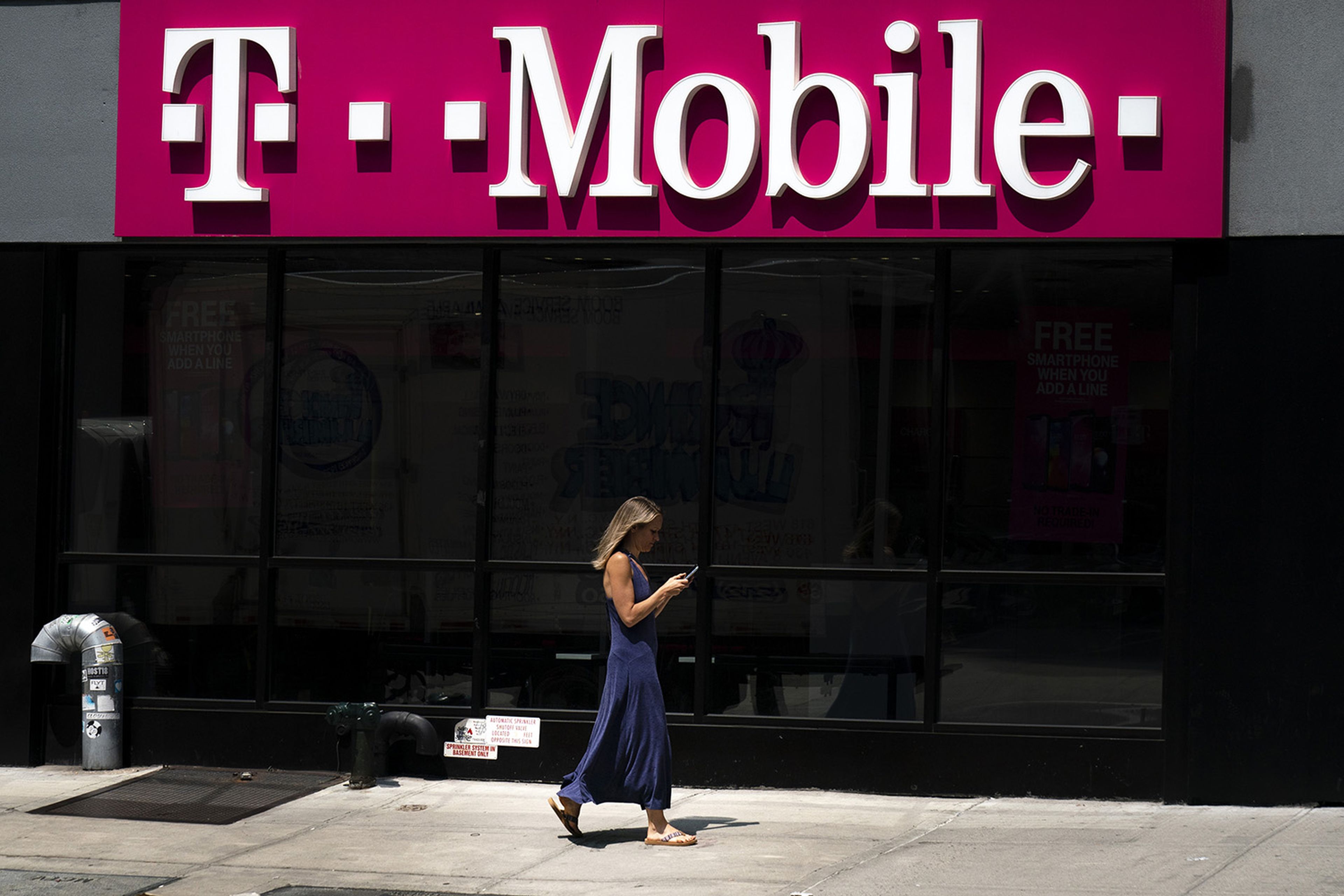 A woman looks on her phone as she walks past a T-Mobile store on Sixth Avenue in Manhattan on July 26, 2019, in New York City. (Photo by Drew Angerer/Getty Images)