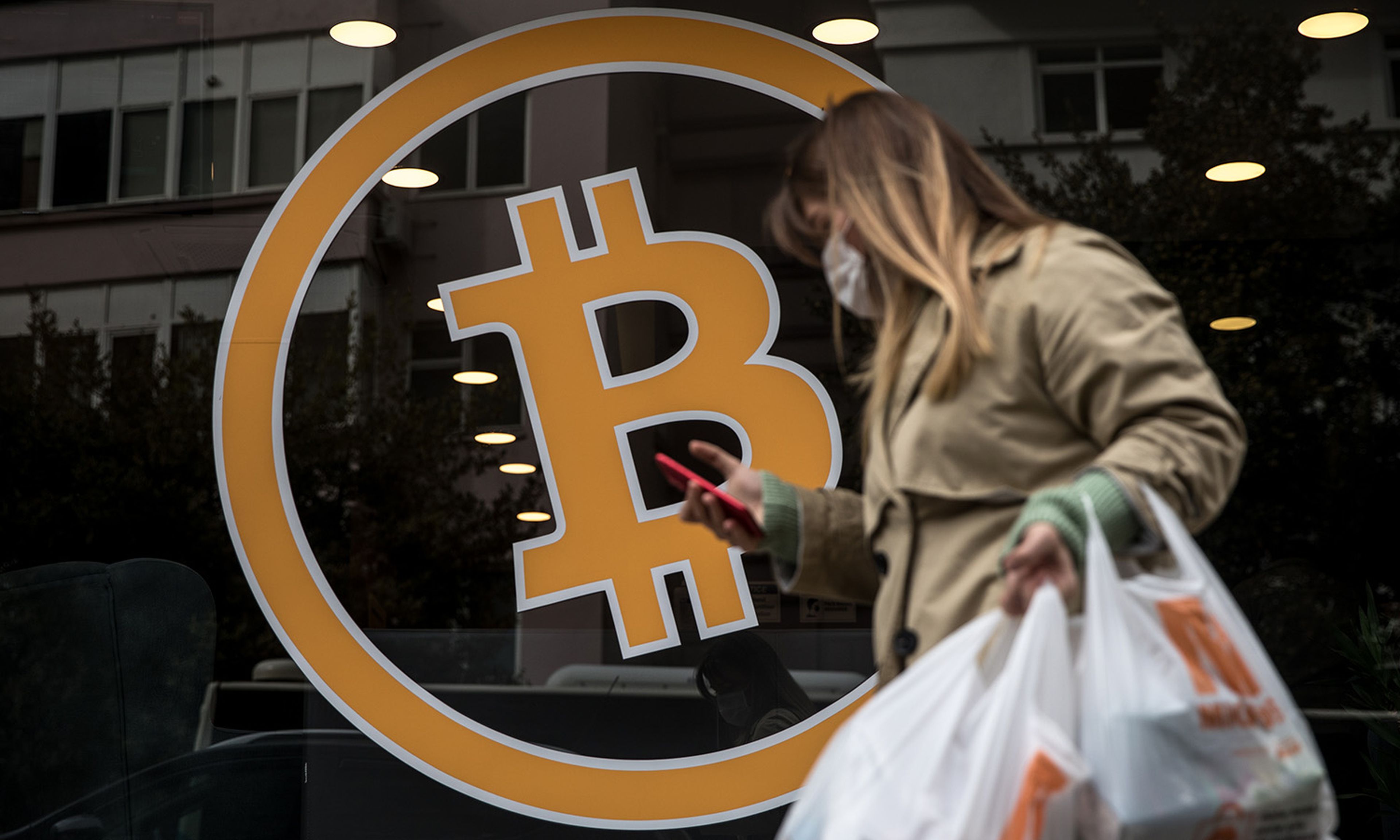 A woman walks past the entrance of a cryptocurrency exchange office on April 16, 2021, in Istanbul. Two new reports detail crypto-mining threats found by Akamai. (Photo by Chris McGrath/Getty Images)