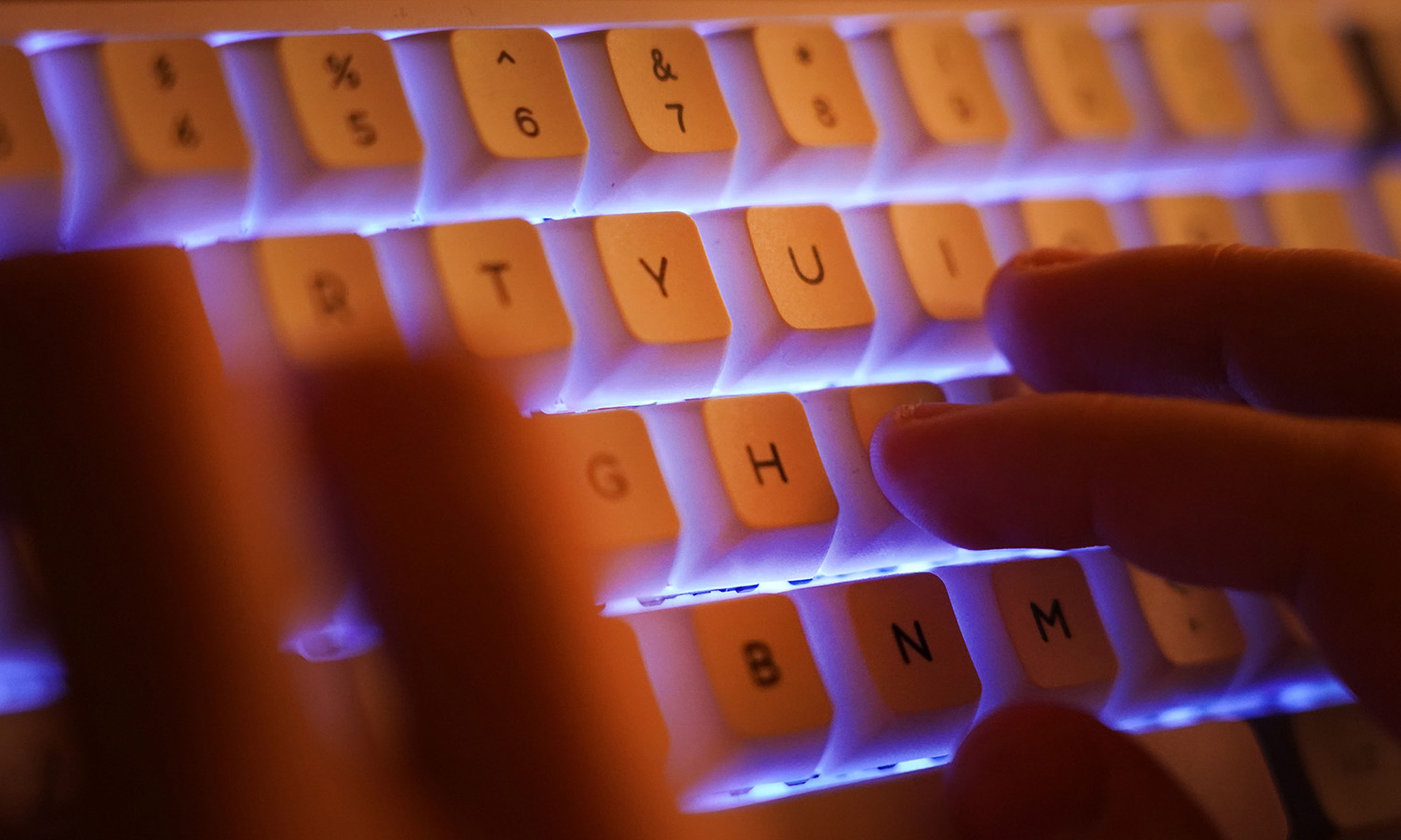 A young man types on an illuminated computer keyboard typically favored by computer coders on Jan. 25, 2021, in Berlin. (Photo by Sean Gallup/Getty Images)