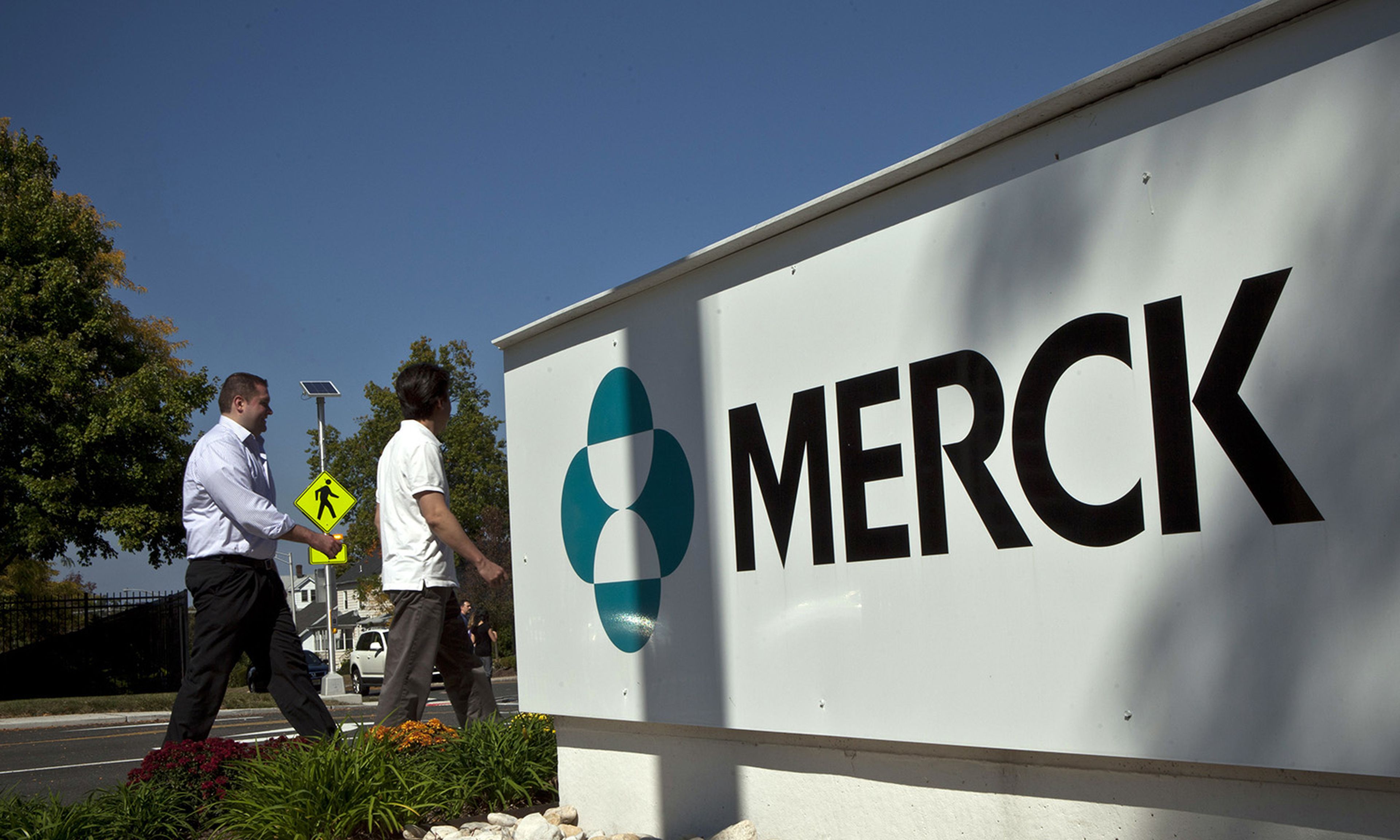 Merck employees walk past a Merck sign in front of the company&#8217;s building on Oct. 2, 2013, in Summit, N.J. (Photo by Kena Betancur/Getty Images)