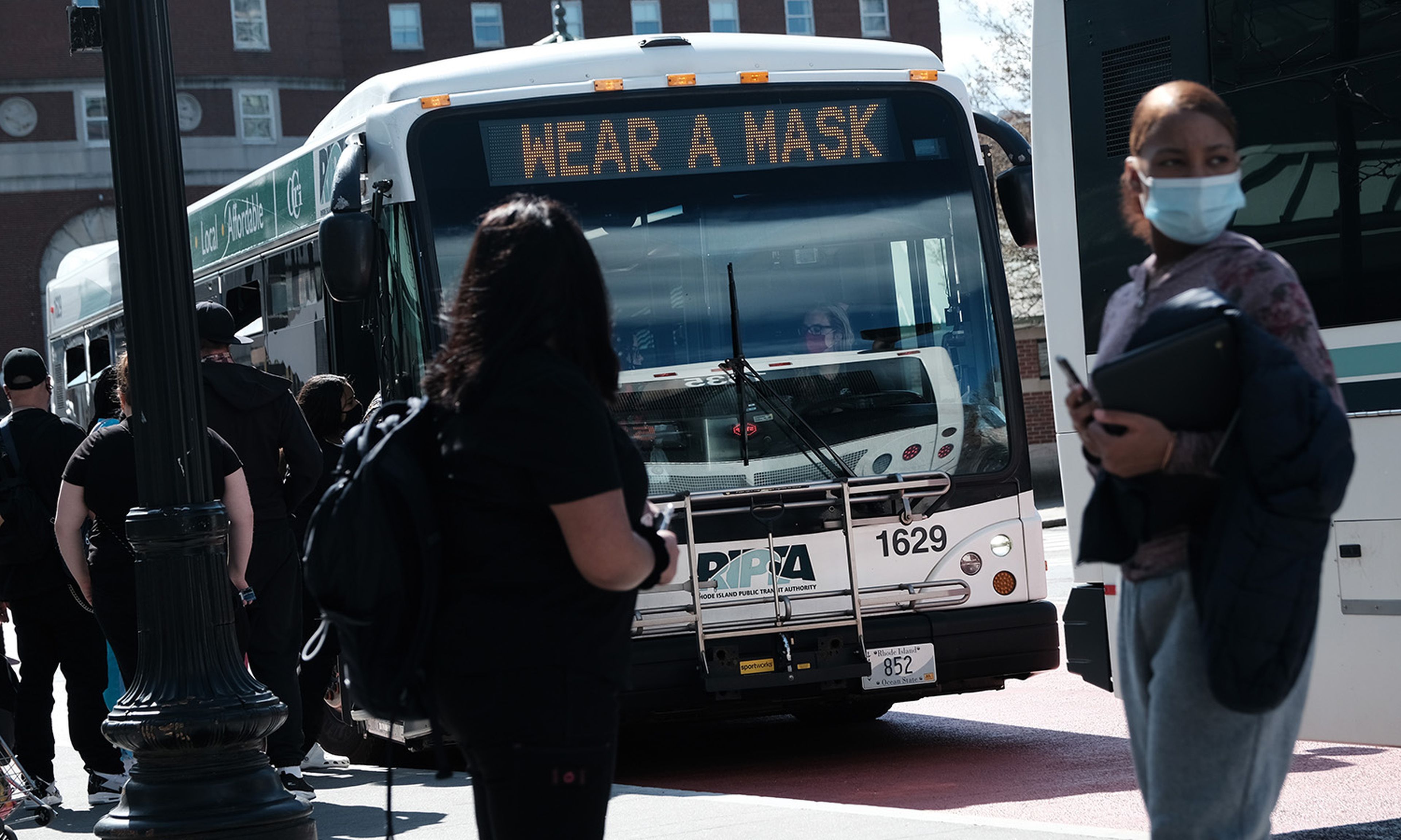 People wait at a bus stop on April 8, 2021, in Providence, R.I. An ongoing investigation into the public transit authority reveals new details, including that its former health plan administrator has been added to the review. (Photo by Spencer Platt/Getty Images)