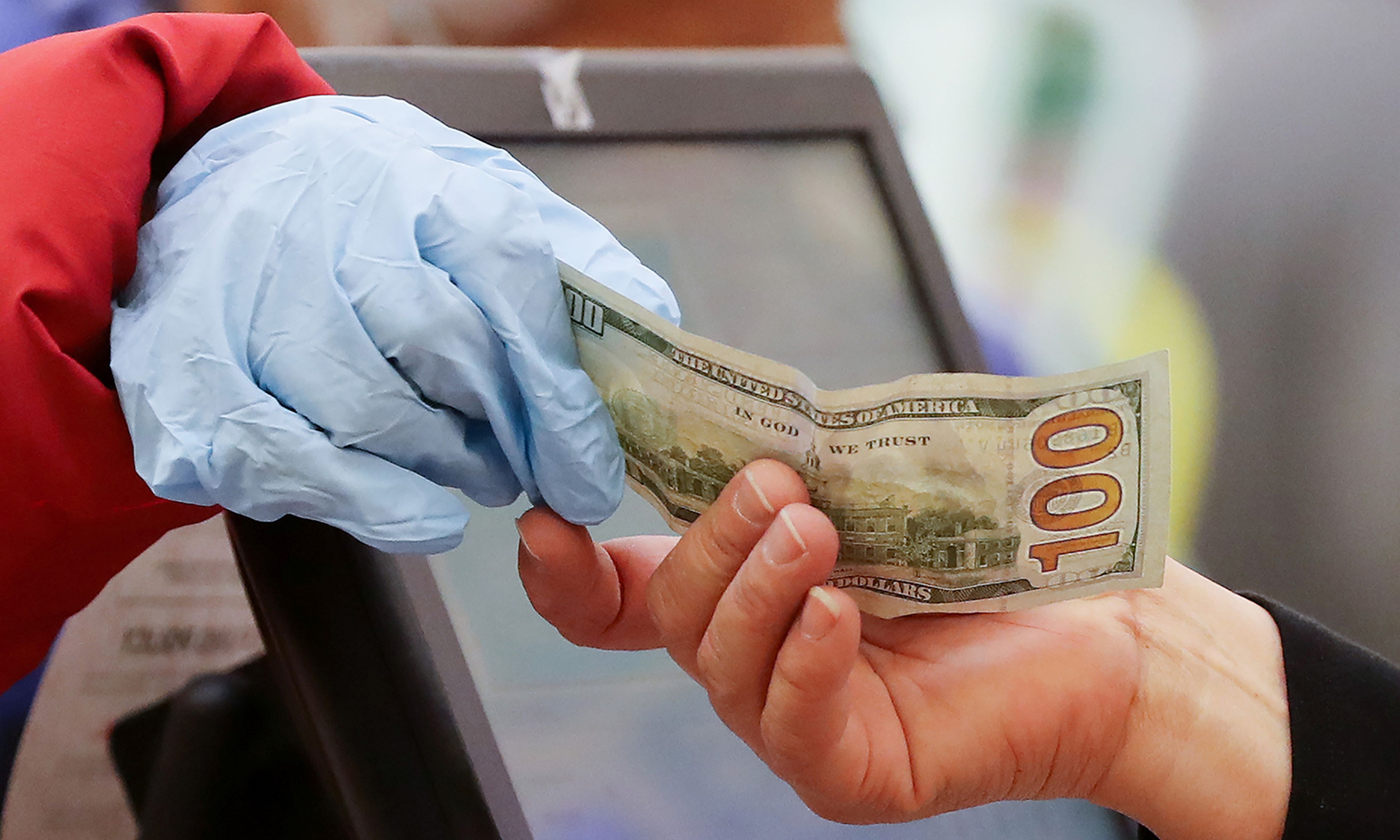 A woman pays cash while wearing gloves at Northgate Gonzalez Market on March 19, 2020, in Los Angeles. (Photo by Mario Tama/Getty Images)