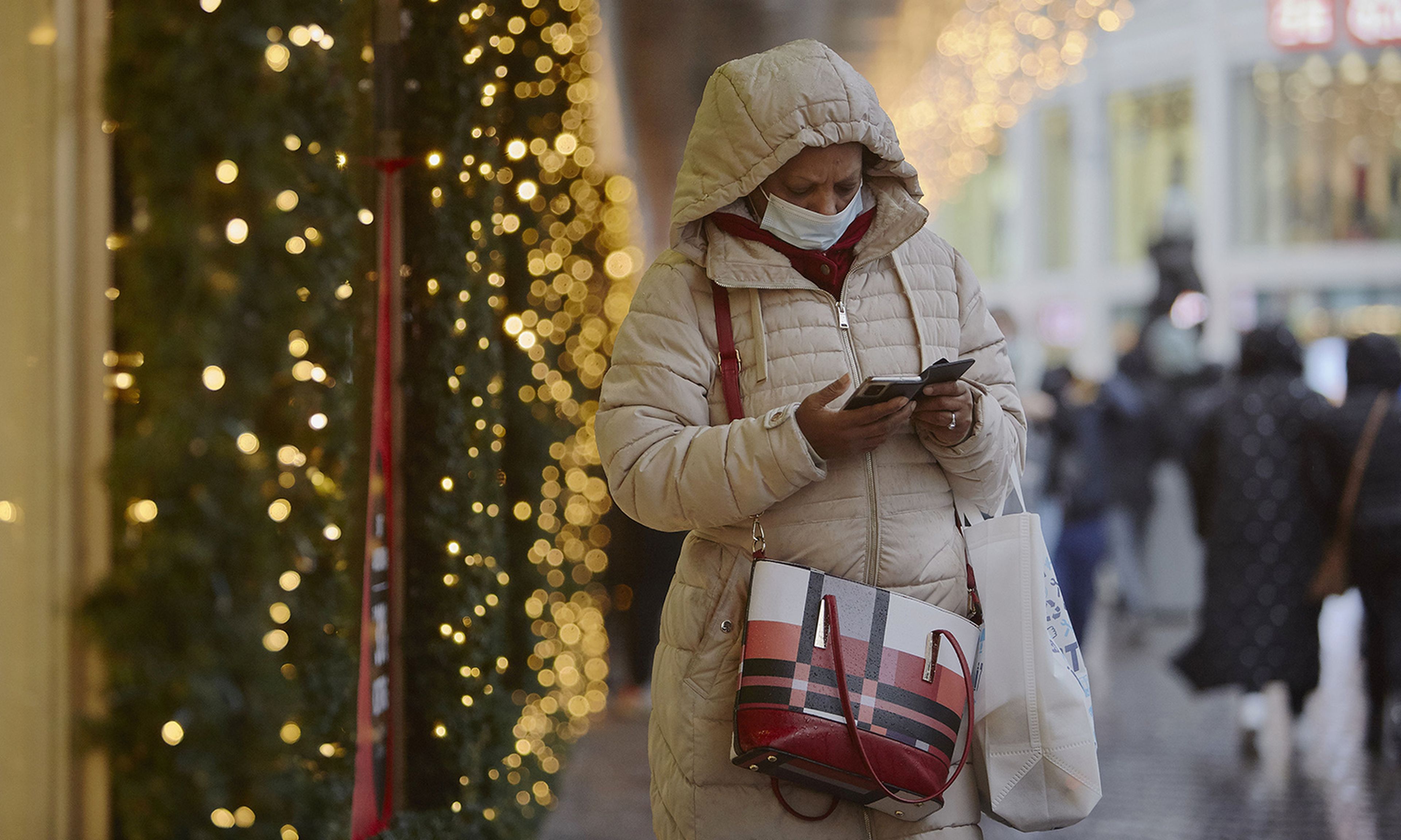 Pictured: A woman wearing a face mask eyes her smartphone outside a store on Black Friday on Nov. 26, 2021, in The Hague, Netherlands. (Photo by Pierre Crom/Getty Images)