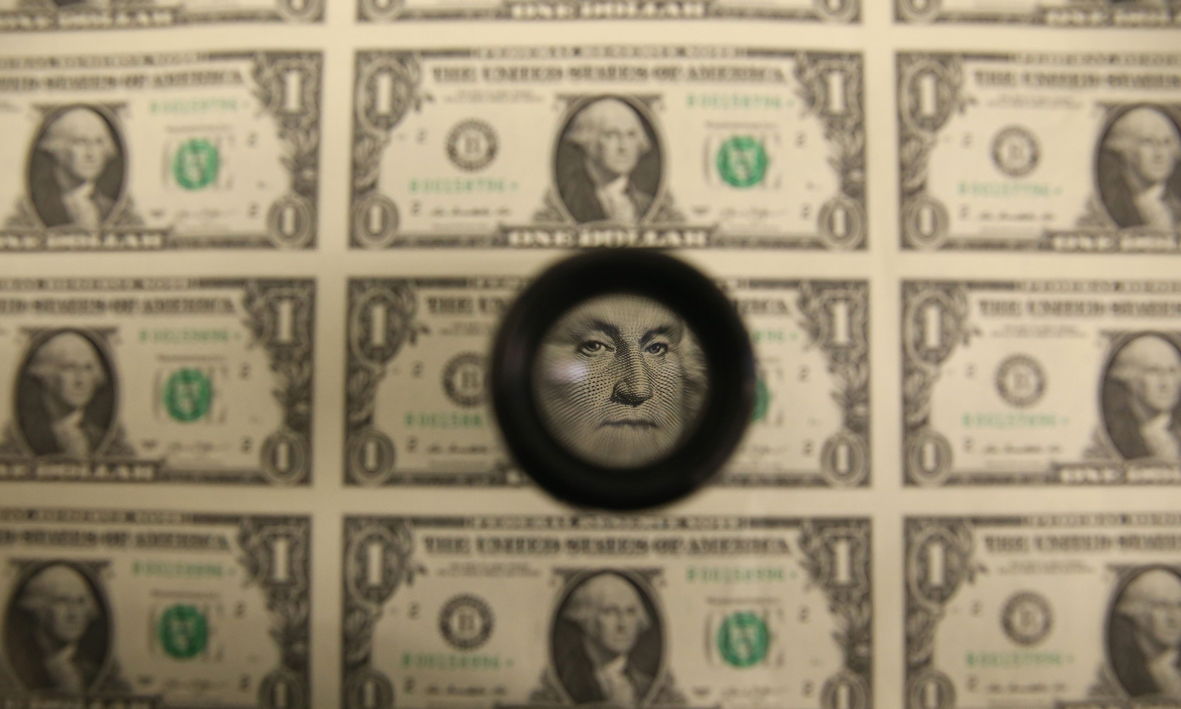 A magnifying glass is used to inspect newly printed one dollar bills at the Bureau of Engraving and Printing on March 24, 2015, in Washington. (Photo by Mark Wilson/Getty Images)