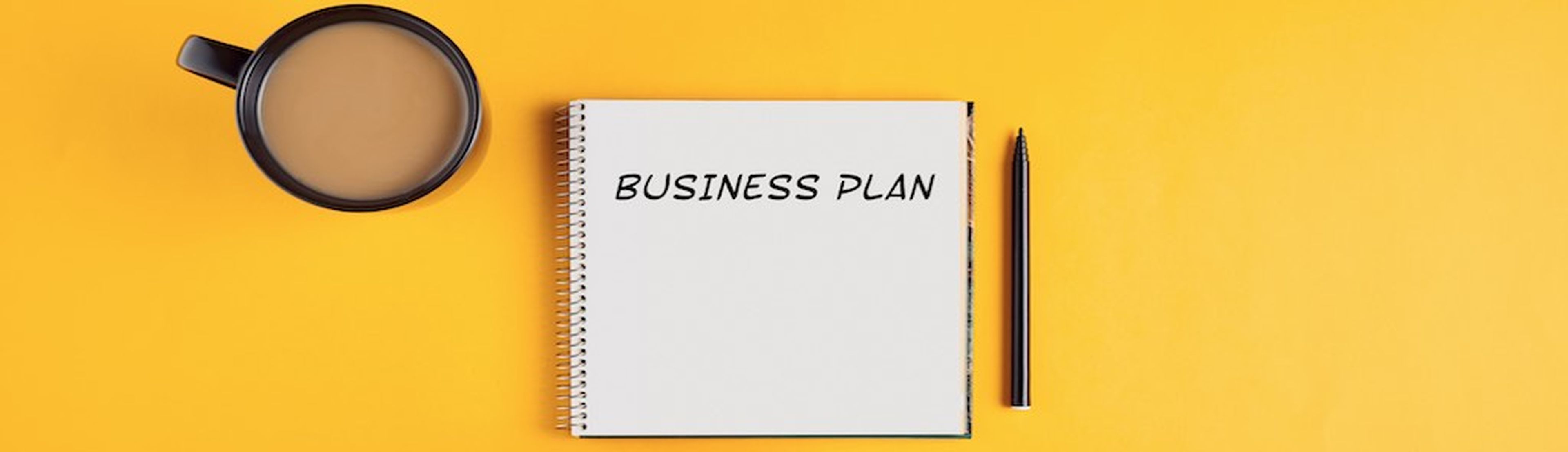 Hands of a businessman with spiral notebook with business plan ideas ready to be written in it. Yellow background with copy space.
