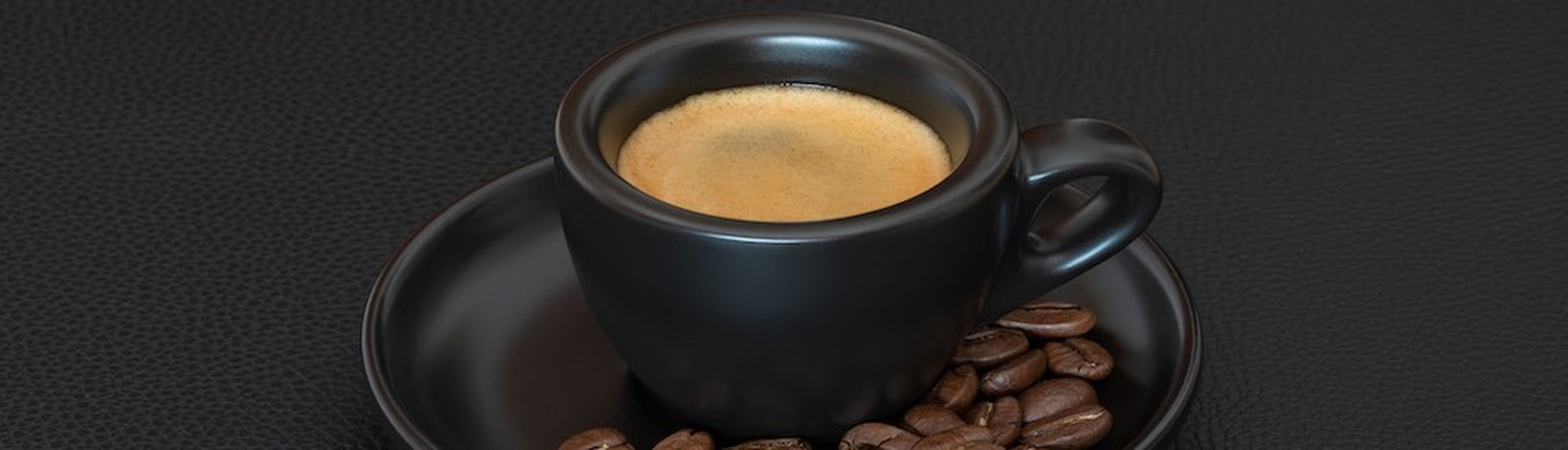 Original italian espresso in black cup on leather background with coffee beans