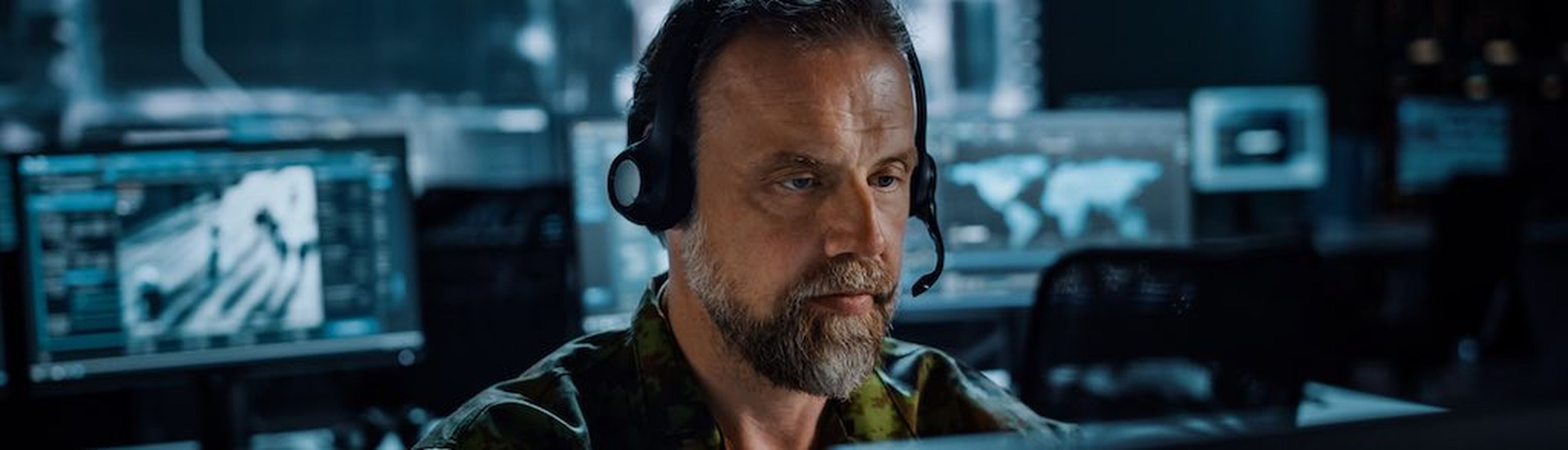 Bearded Military Surveillance Officer in Headset Working in a Central Office Hub for Cyber Operations, Control and Monitoring for Managing National Security, Technology and Army Communications. (Bearded Military Surveillance Officer in Headset Working