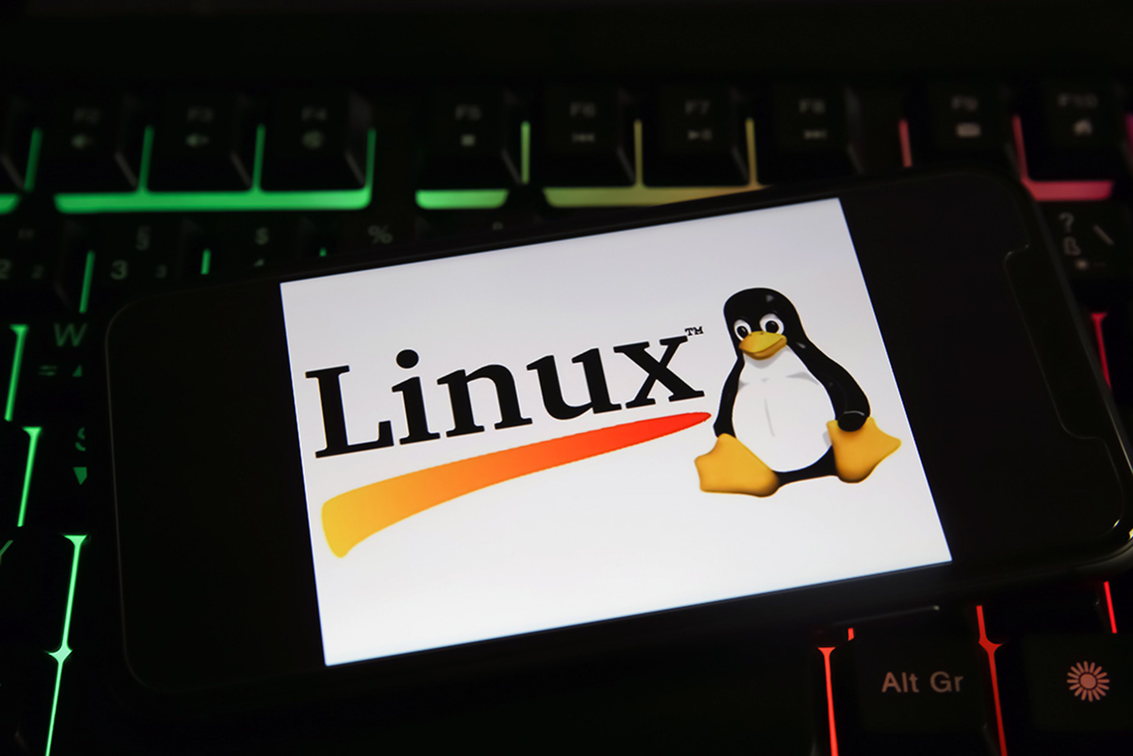 Closeup of a mobile phone screen with logo lettering of linux on computer keyboard