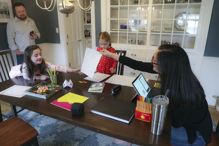 A Boston-area mother does work on a conference call while helping her two daughters with schoolwork. (Matthew J. Lee/The Boston Globe via Getty Images)