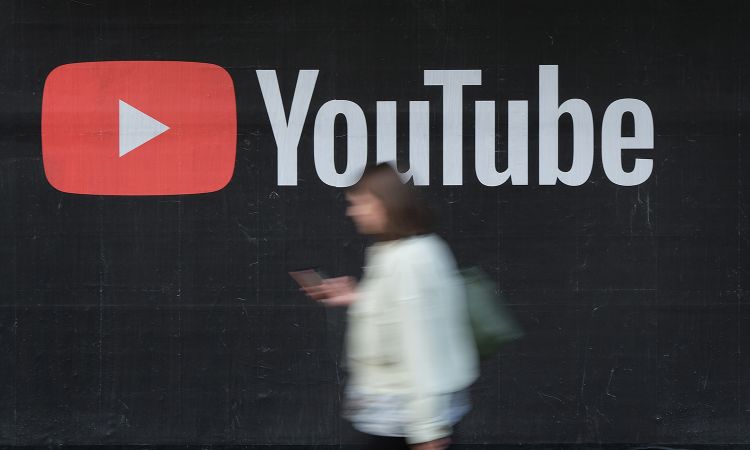 A young woman with a smartphone walks past a billboard advertisement for YouTube.