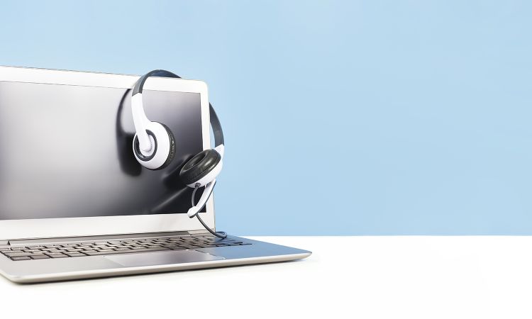 Laptop with blank screen with headphones on white desk blue background and copy space