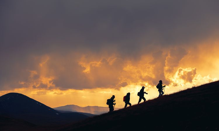 Group of unrecognizable hikers are walking at majestic sunset in mountains